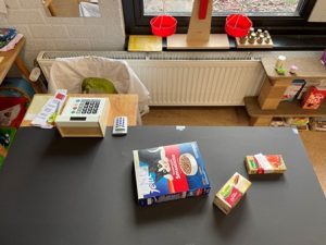 Spelhoek - In de supermarkt Maak een supermarkt in je lokaal. Denk bij de inrichting van de winkel aan: reclameposters, schappen of een kast met daarin dozen van levensmiddelen, AH-mini's, kunststof fruit en groenten in bakken gesorteerd, een weegschaal, een kleine winkelwagen, een boodschappentas, een speelgoedkassa, geld, portemonnee, een schort (bedrijfskleding) een tafel waarop papier en een potlood of stempels liggen voor het maken van boodschappenlijstjes, kassabonnen enzovoorts. Laat de winkelmedewerkers de producten prijzen. De klanten wegen het fruit en de groeten met de weegschaal. Hiervoor kun je eventueel ook gewichten gebruiken (balansweegschaal). Nummer de gewichten. Het fruit kost zoveel als het cijfer op het gewicht gelijk aan het gewicht van het fruit. Laat kinderen de reclameposters maken door afbeeldingen uit reclamefolders van supermarkten te knippen, te stempelen of te schrijven. Laat ook enkele kinderen zelf reclamefolders voor jullie supermarkt maken en in de huishoek verspreiden. --> Download de lege reclameposters